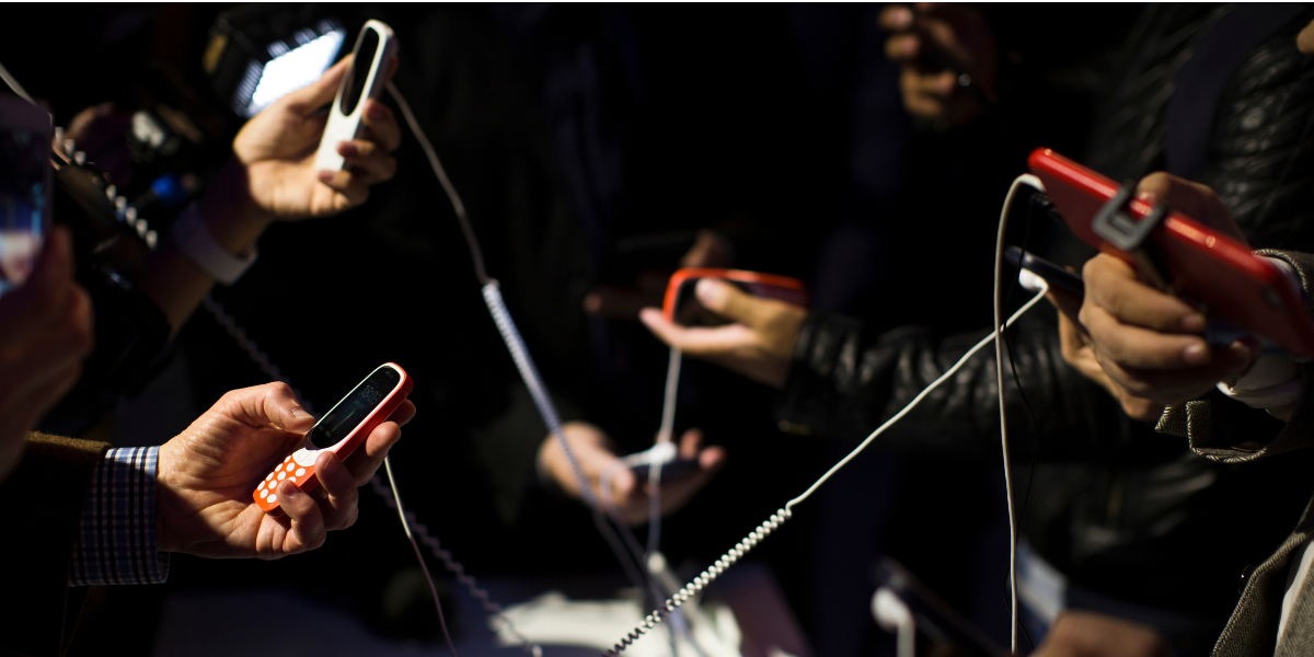 Flera människor håller i gamla mobiltelefoner med sladdar mellan sig.