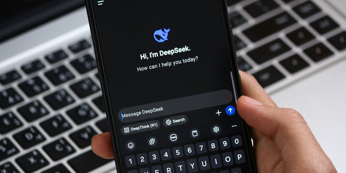 En mobiltelefon med Deepseeks startsida uppe framför en dator.